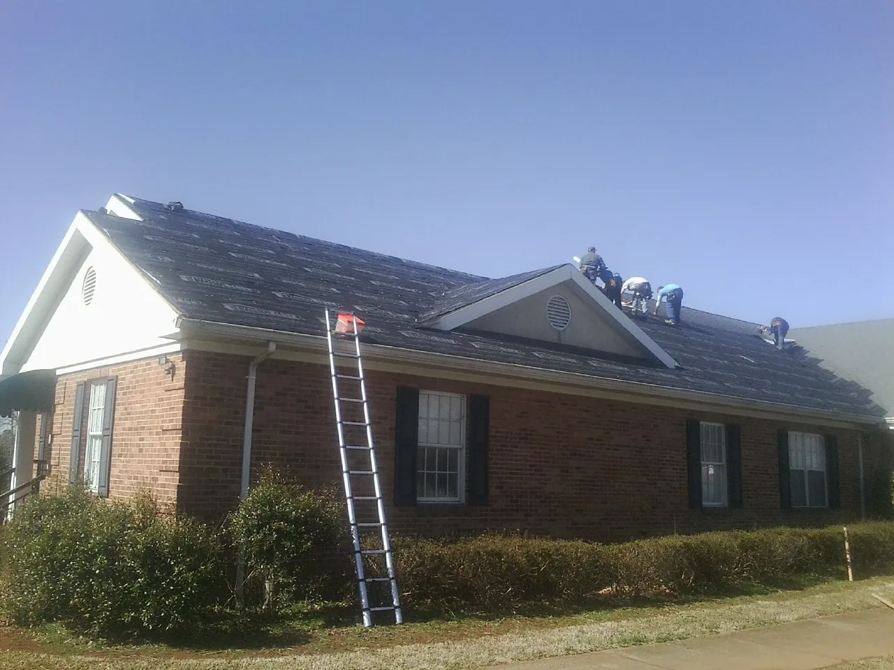 Crew tearing shingles off a brick ranch roof with a ladder set — Emergency Roof Repair work by our crew in Carson